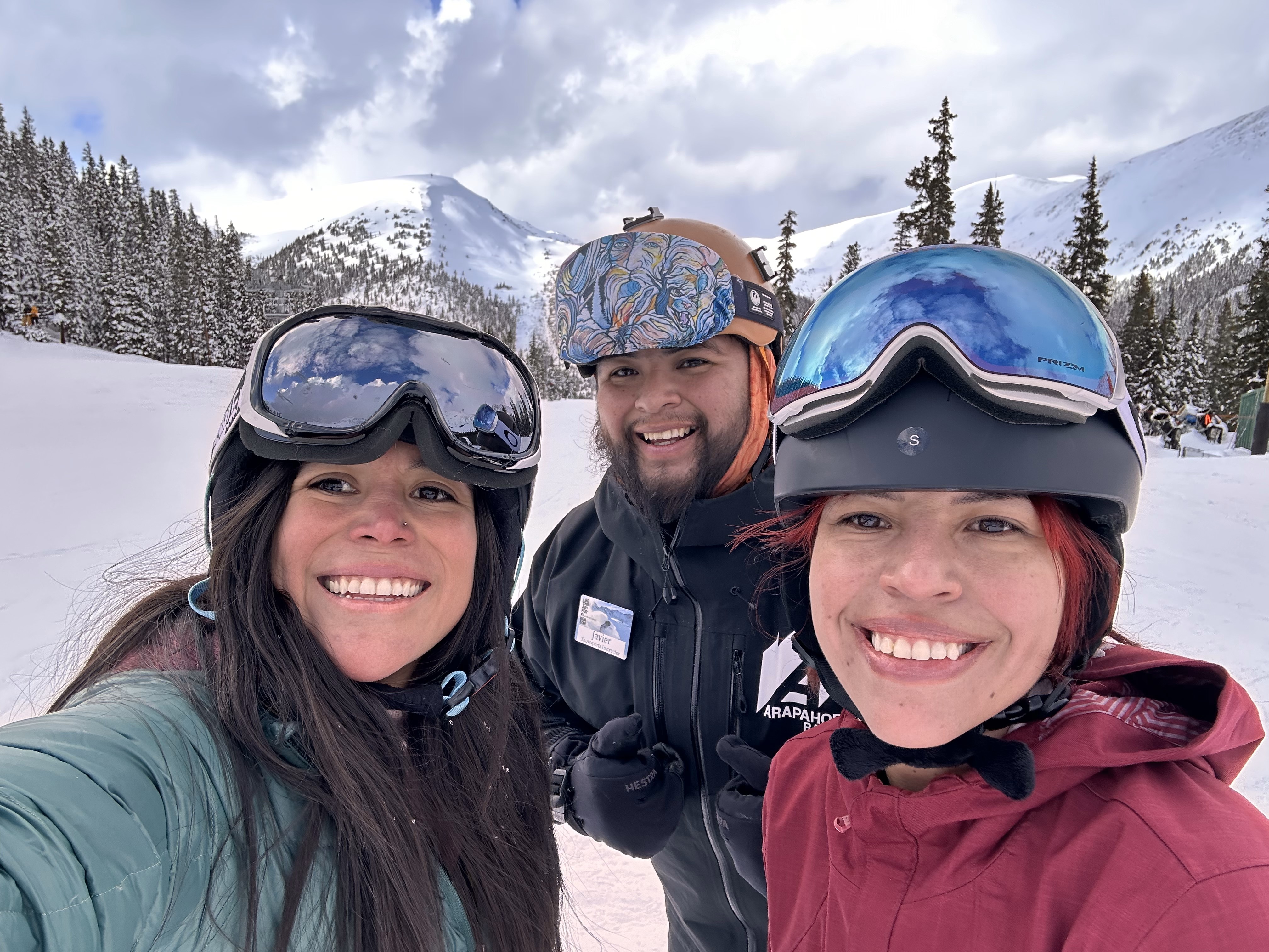 Three people wearing snow gear look into the camera and smile